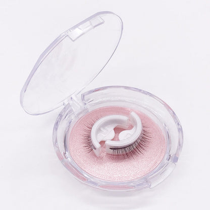 Open clear round case showing a pair of self-adhesive lashes on white curved holders over a pink glittery tray, on a white background. 6