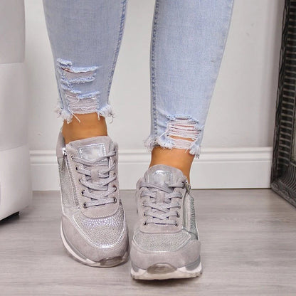 Front view of grey lace-up trainers on a model, showing the laces, studded panels and side zips on both shoes. 5