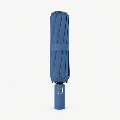 Folded denim blue umbrella standing handle-down on a white background, with a matching strap and a metallic square on the handle. 11