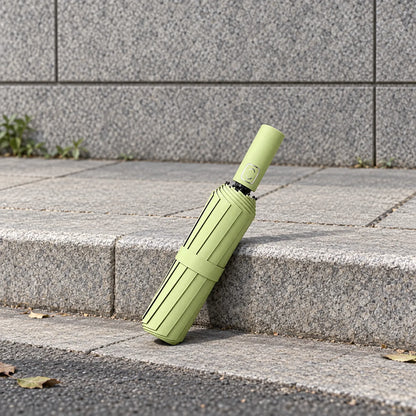 Folded lime green umbrella leaning against a granite kerb on a paved street, shown in an everyday outdoor setting. 3