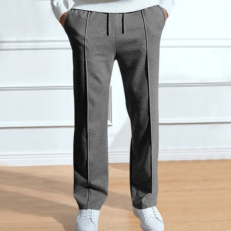 Front view of the trousers in mid-grey on a model with hands in pockets, showing drawstring and central creases, with white trainers. 2