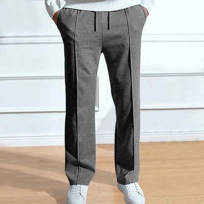 Front view of the trousers in mid-grey on a model with hands in pockets, showing drawstring and central creases, with white trainers. 2