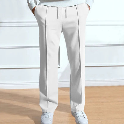 Front view of the trousers in white on a model, with drawstring waist, front pleat lines and hands in pockets, worn with white trainers. 4