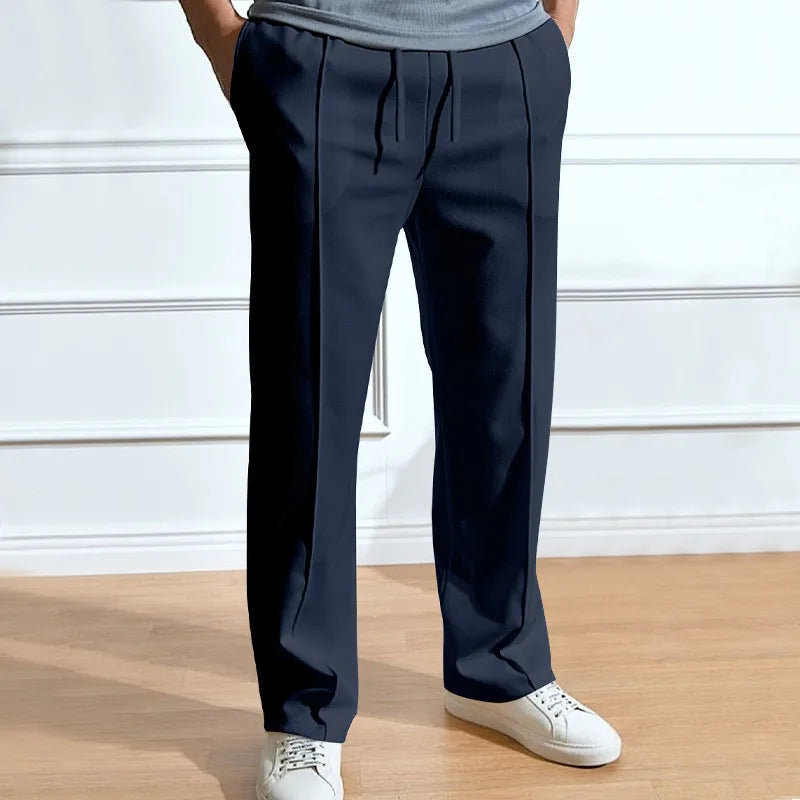 Model wearing the trousers in navy with hands in pockets, drawstring waist and front pleat lines, styled with white trainers. 1
