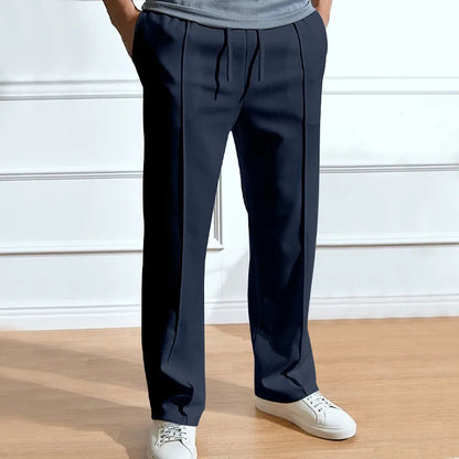 Model wearing the trousers in navy with hands in pockets, drawstring waist and front pleat lines, styled with white trainers. 1