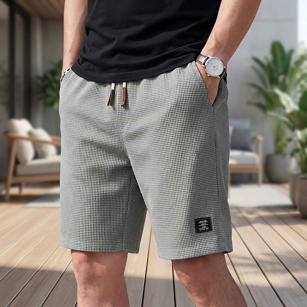 Model wearing grey waffle-textured shorts with a drawstring waist and small woven label, one hand in a pocket, on a terrace. 6