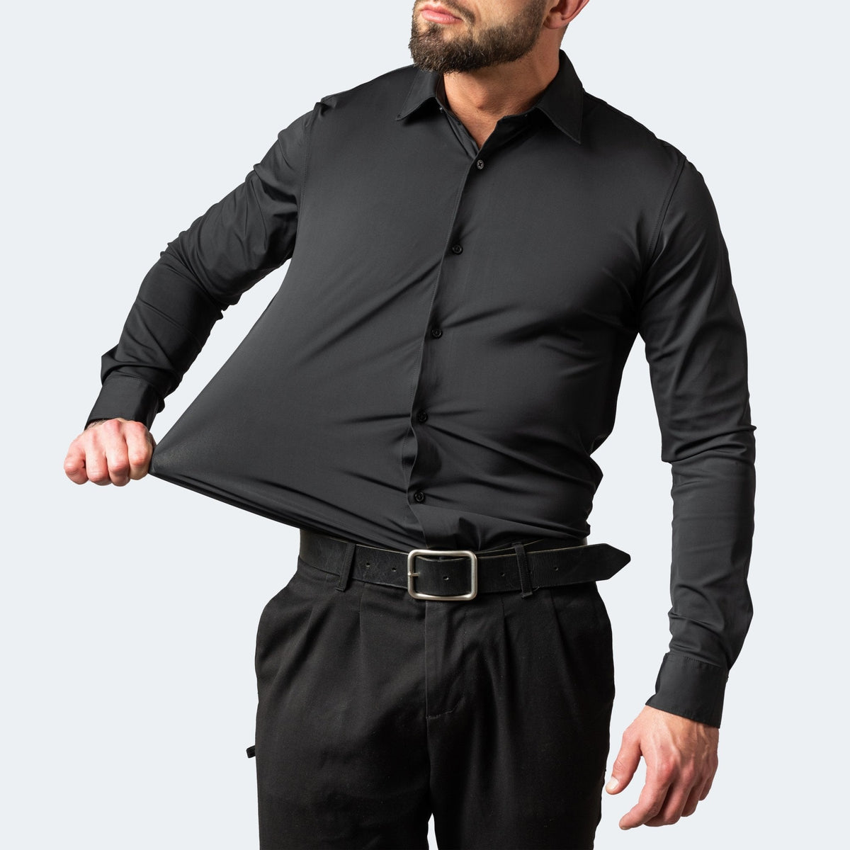 Man in a black shirt with dark trousers pulling the stretchy fabric out from his waist 4