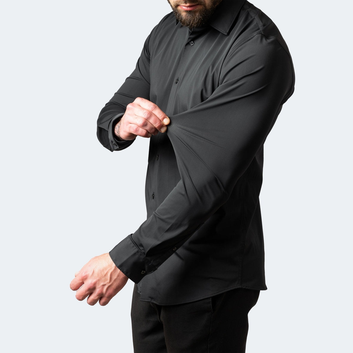 Black shirt on a model, one hand pinching and stretching the sleeve fabric outwards 6
