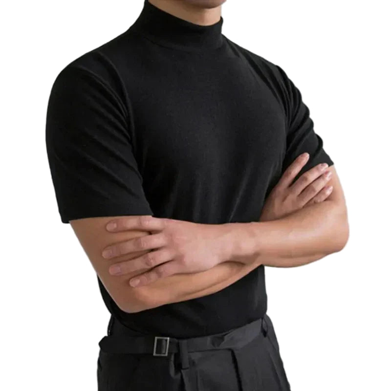 Model with arms crossed wears the black short-sleeved high-neck t-shirt tucked into dark trousers, on a plain white background. 1