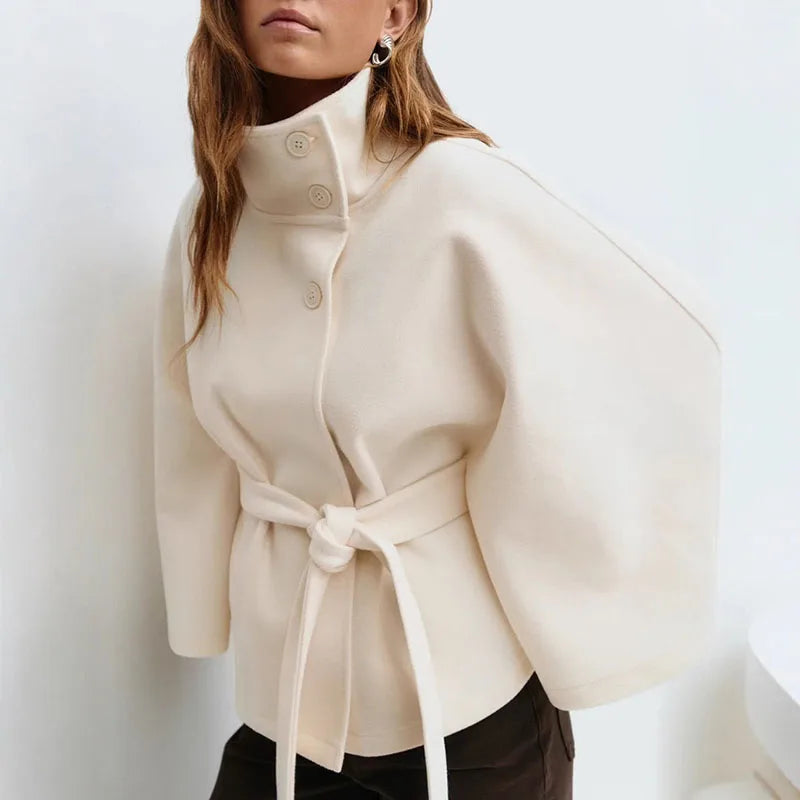 Model wearing the cream cape jacket with a knotted belt, dark trousers and silver earrings 3
