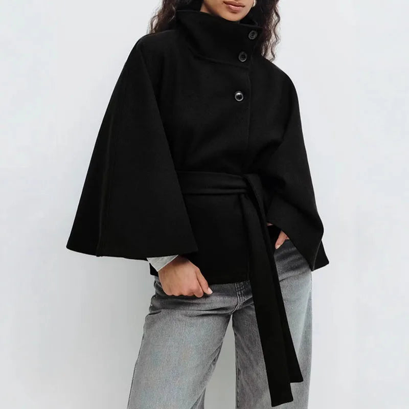Model wearing the black cape jacket with grey jeans, hands in pockets, belt tied 5