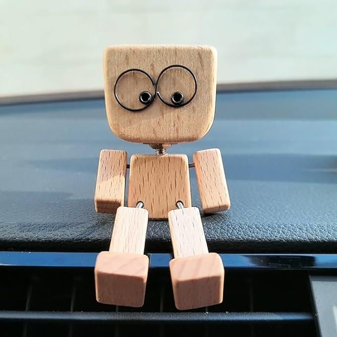 Front view of the wooden figure on a dashboard, big round wire eyes, arms at its sides and legs hanging down. 4