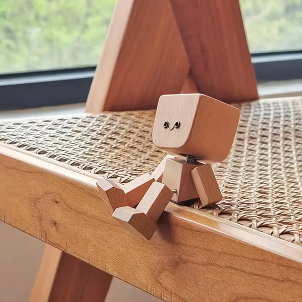 Wooden figure with a small smiling face sitting on the edge of a woven cane chair seat. 5