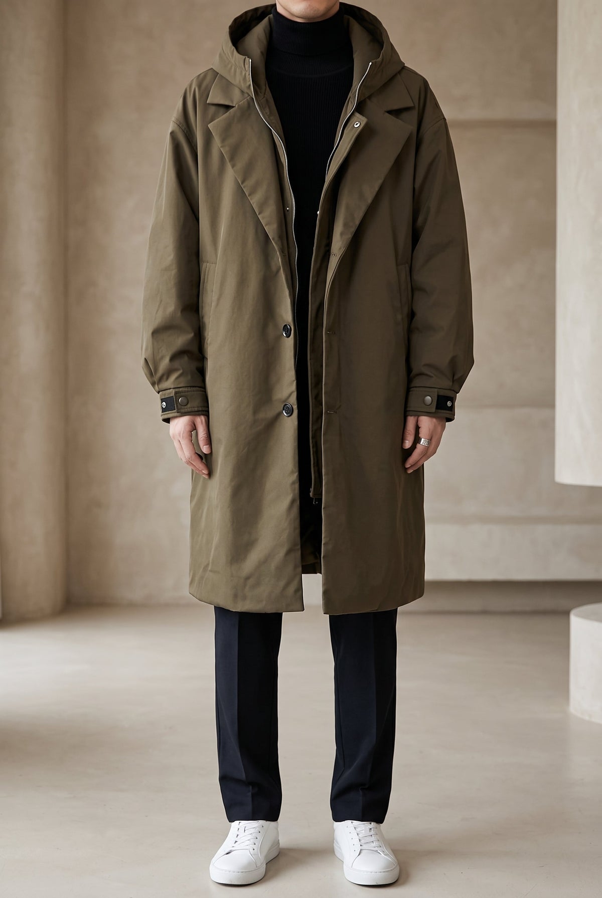 Full-length front view of a model wearing the olive green hooded raincoat open with white trainers 2