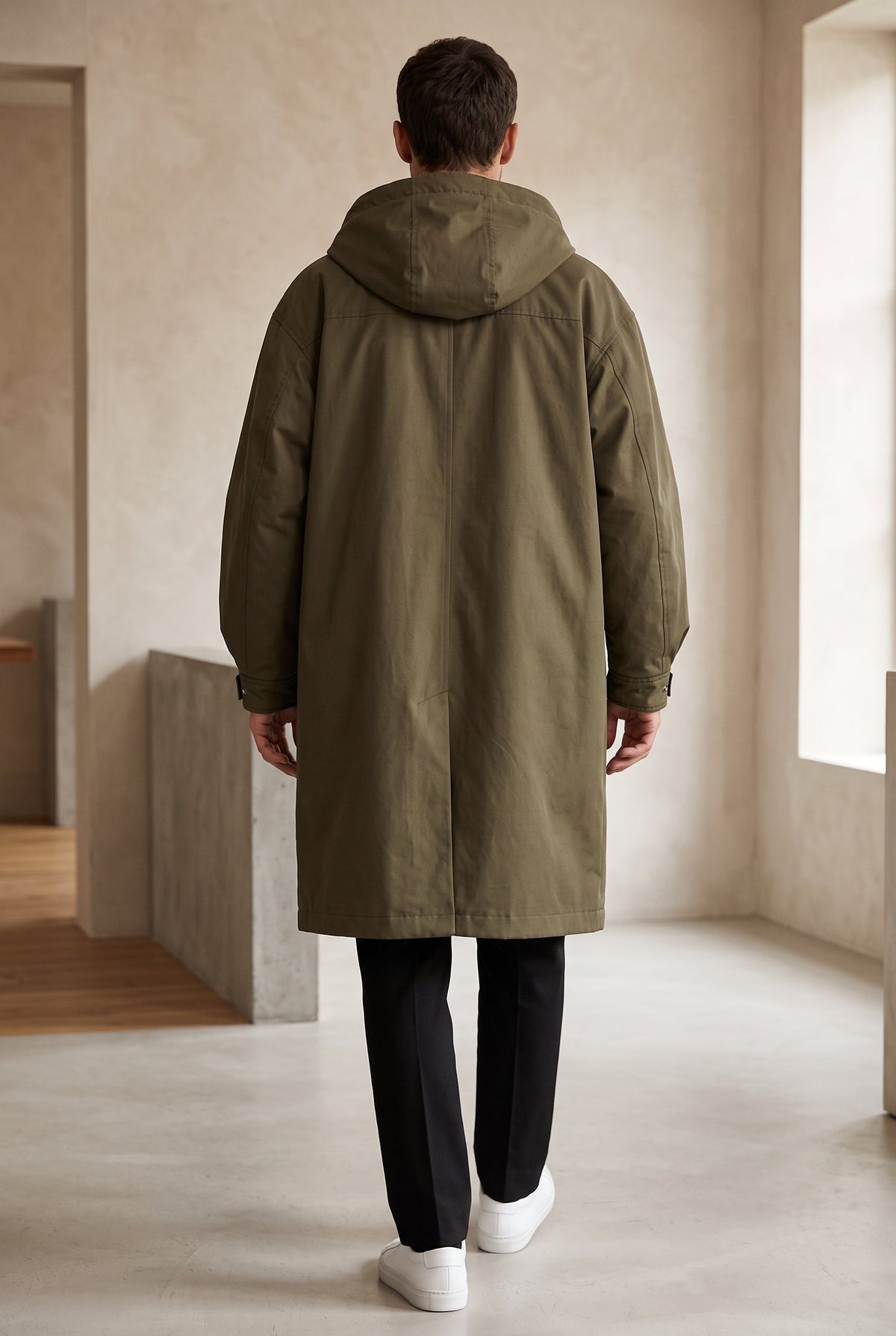 Back view of a model walking in the olive green hooded raincoat, showing the hood and centre seam 3