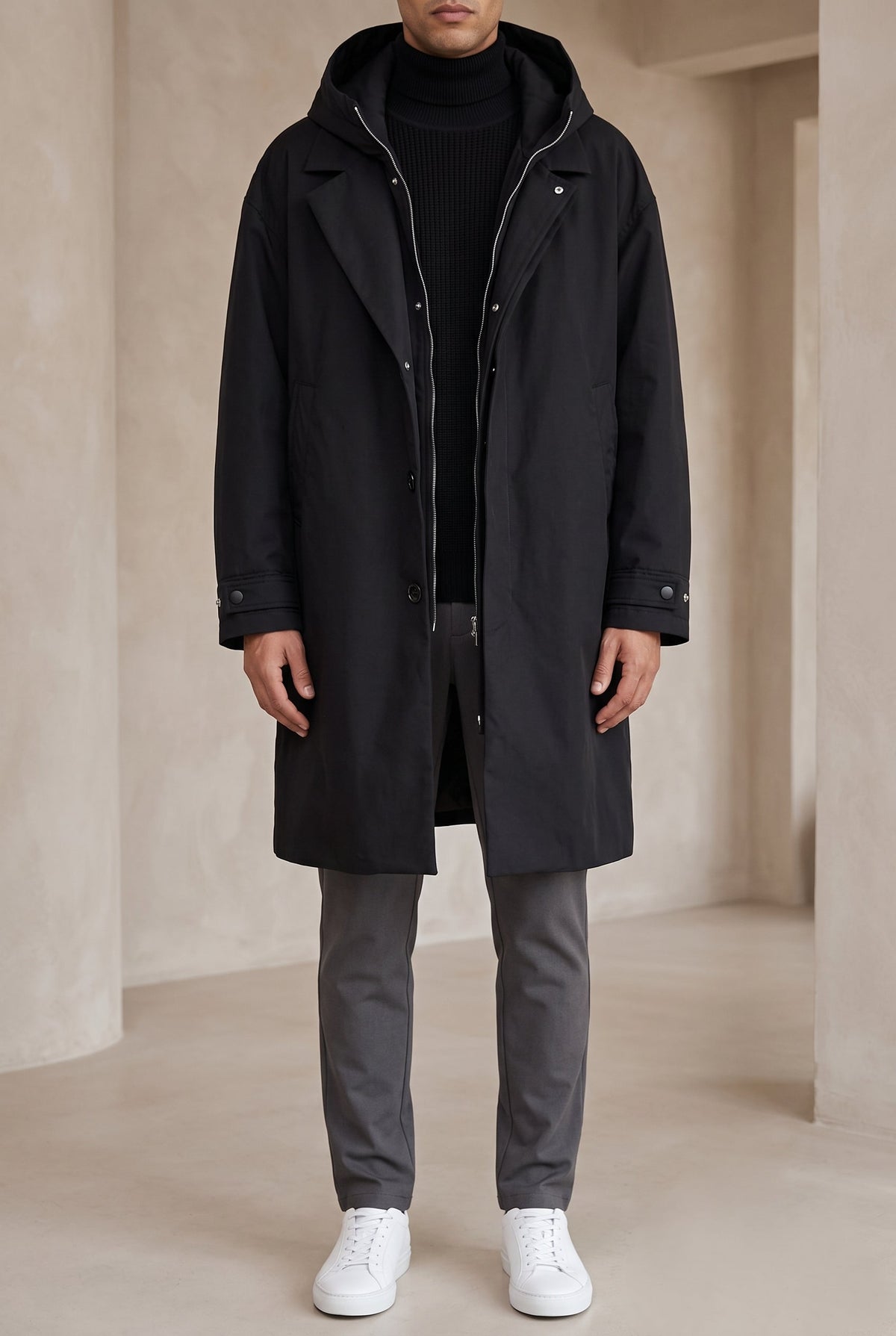 Full-length front view of a model wearing the black hooded raincoat open over grey trousers 6