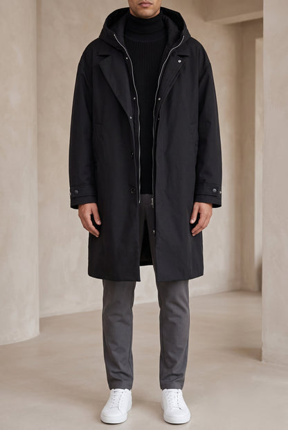 Full-length front view of a model wearing the black hooded raincoat open over grey trousers 6