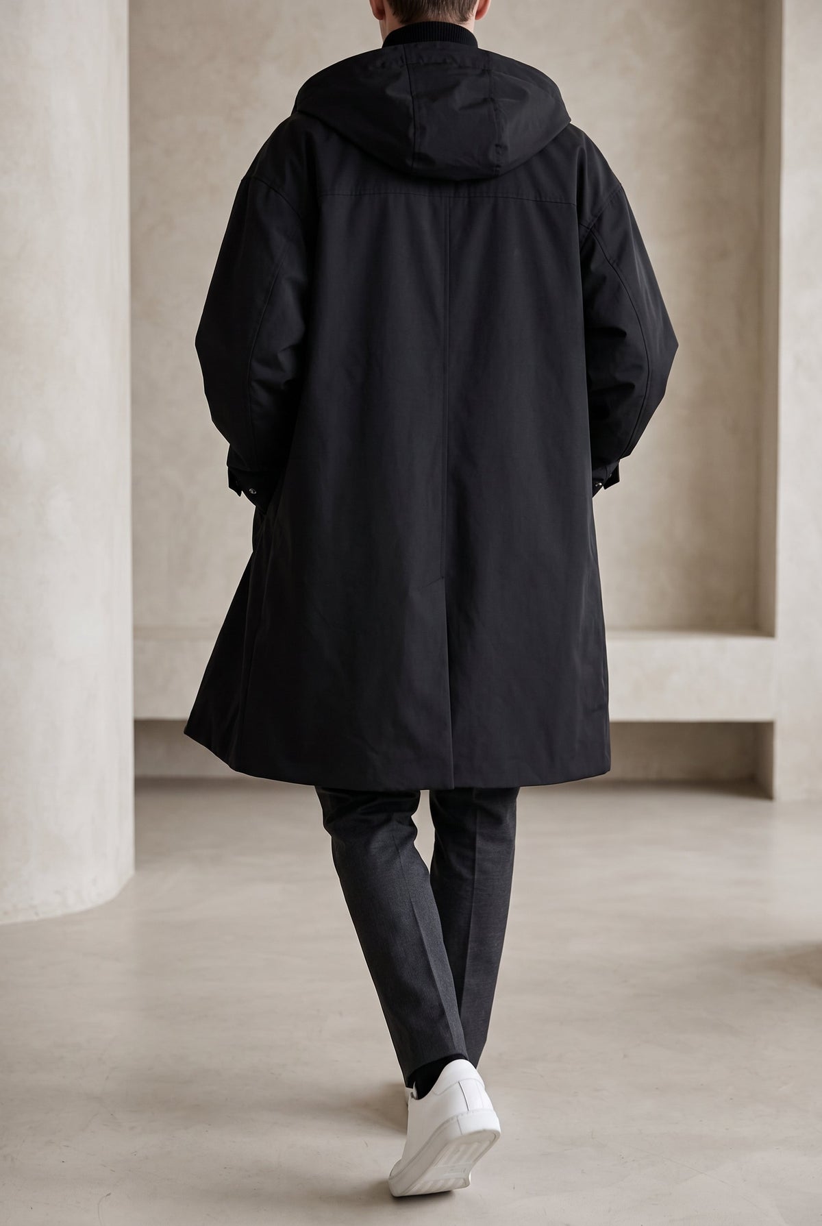 Back view of a model walking in the black hooded raincoat, showing the hood and rear vent 7