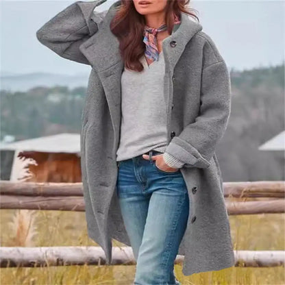 Woman wearing a grey fleecy hooded coat over a grey top and jeans, hand raised to her head 2