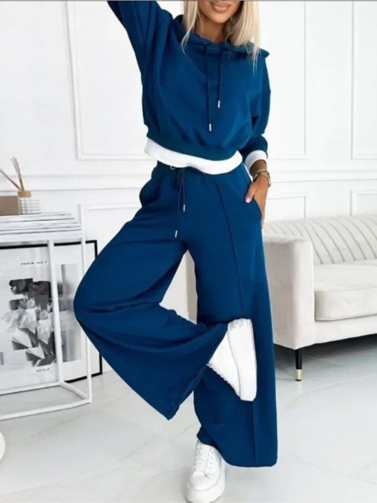 Model in a deep blue hoodie and wide-leg trousers, one arm raised and one leg lifted 3