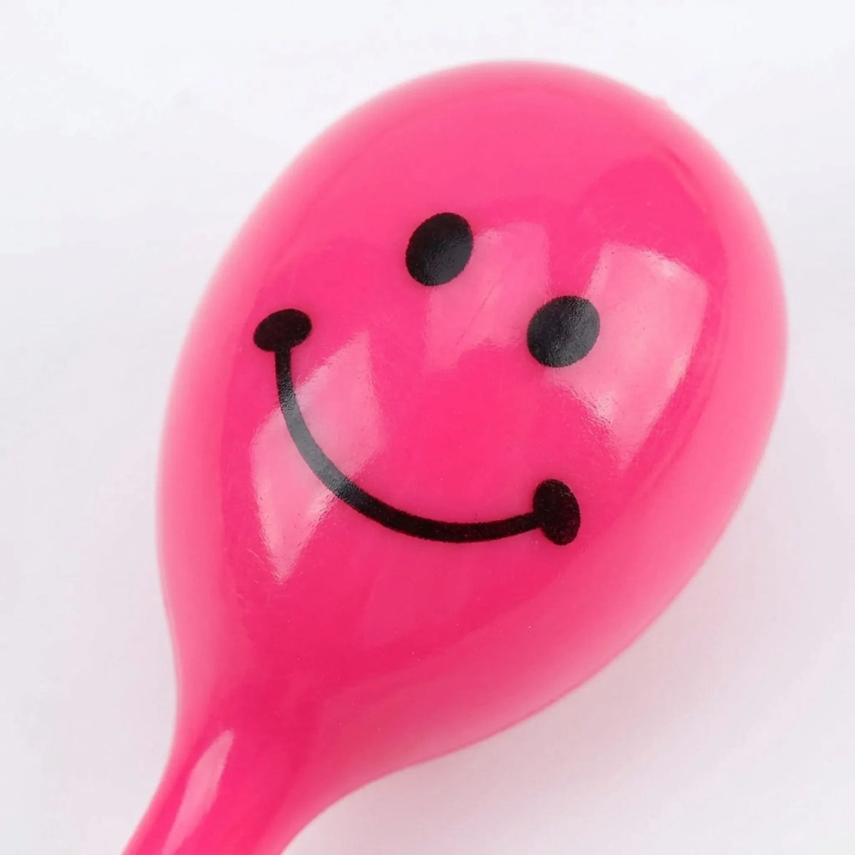 Close-up of the rounded head of a glossy pink maraca with a black smiley face printed on it. 3