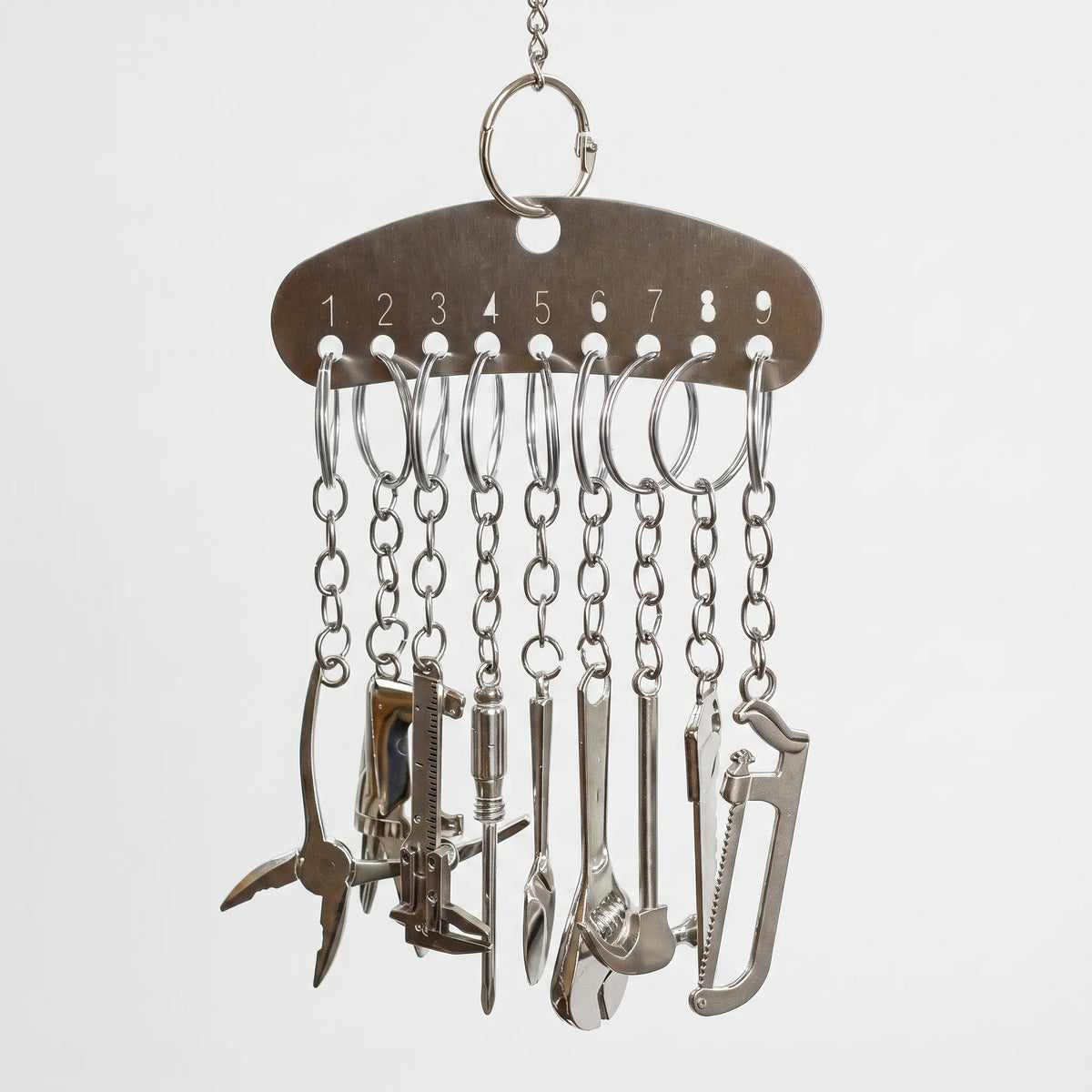 Metal bar hanging from a chain, with nine small chains each carrying a miniature silver tool such as pliers, a saw and a wrench. 1