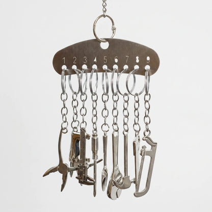 Metal bar hanging from a chain, with nine small chains each carrying a miniature silver tool such as pliers, a saw and a wrench. 1