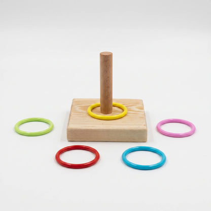 Wooden square base with an upright peg and a yellow ring in place, with green, pink, red and blue rings laid around it on white. 1