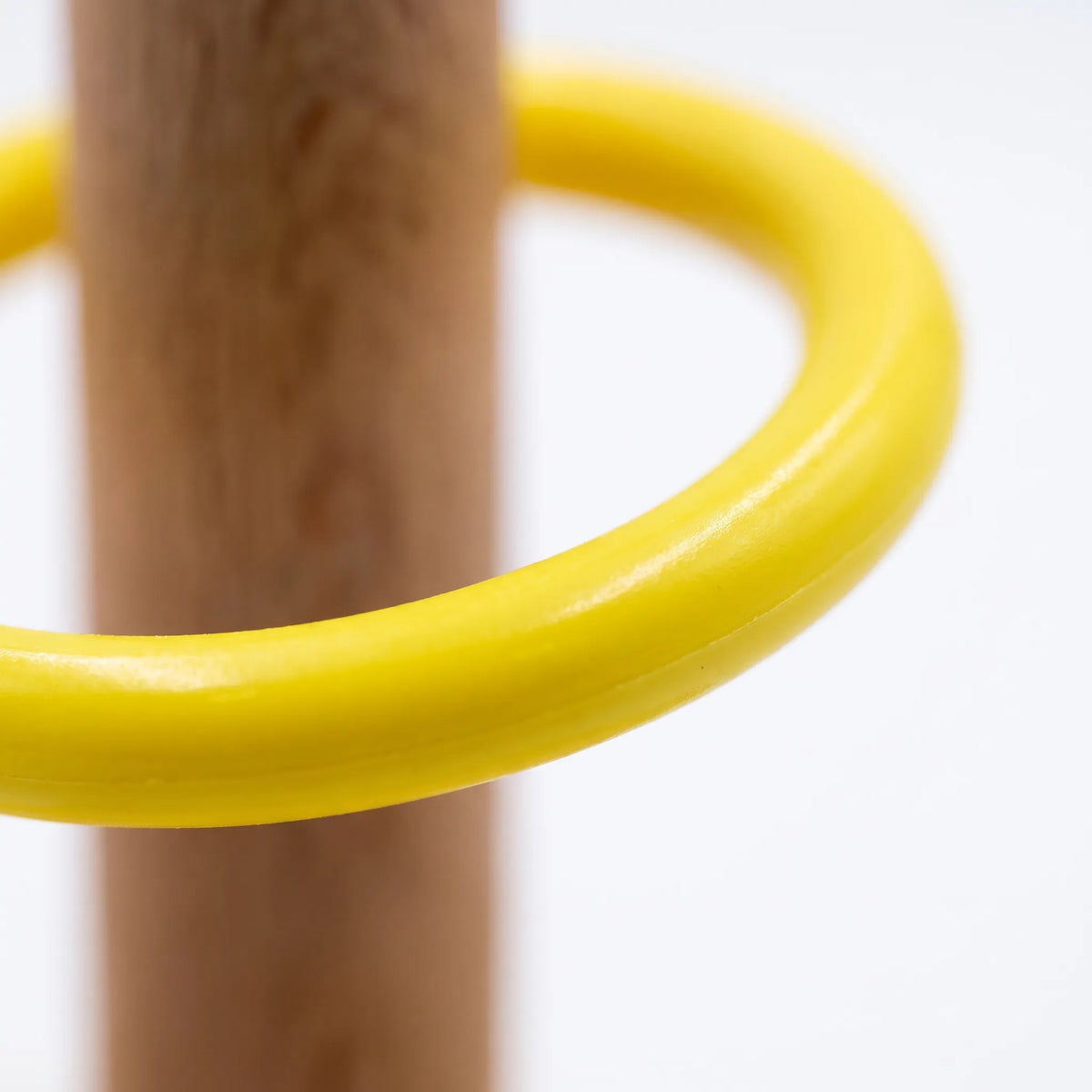 Close-up of a smooth glossy yellow plastic ring resting around the natural wooden peg, showing the finish of the ring. 4