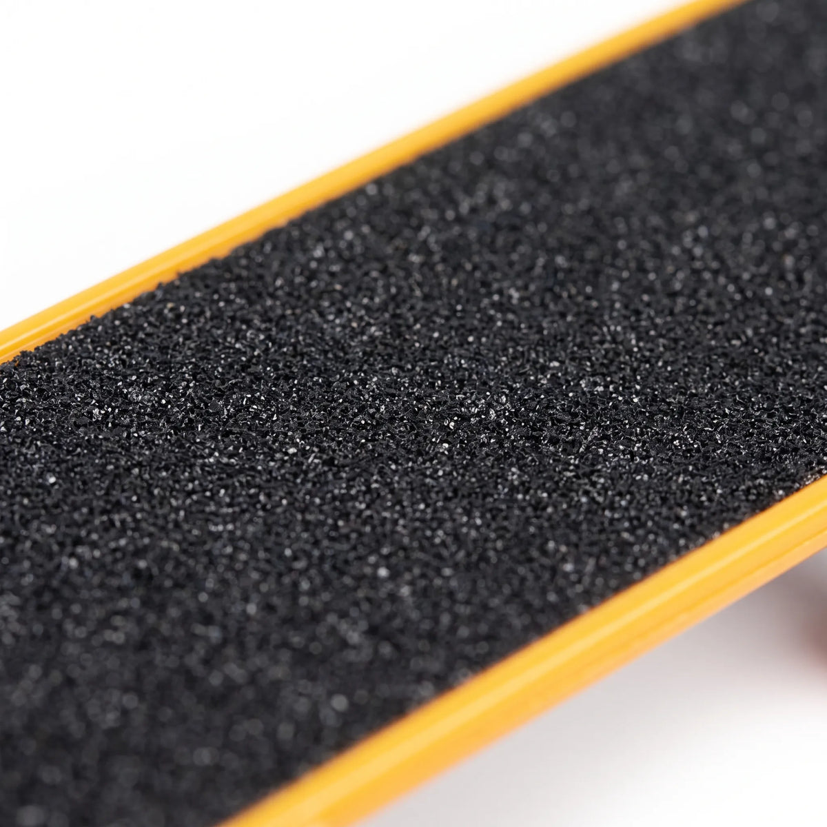 Close-up of the rough black gritty deck surface and yellow rim of the miniature skateboard. 3
