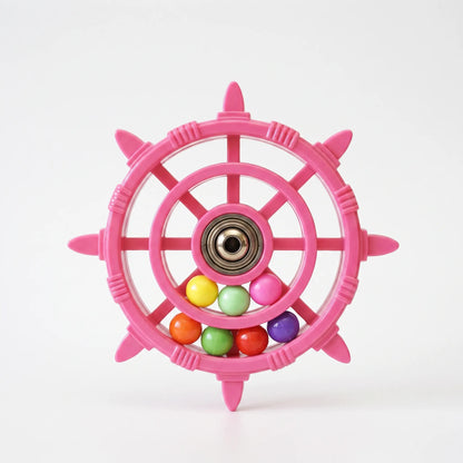 Pink ship's-wheel bird toy with a metal bearing at the hub and loose coloured balls in the rim, shown on plain white. 1