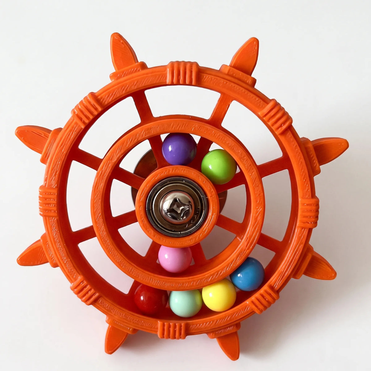 Orange version of the wheel toy with textured, ridged plastic, a metal bearing hub and multicoloured balls in the rings. 5