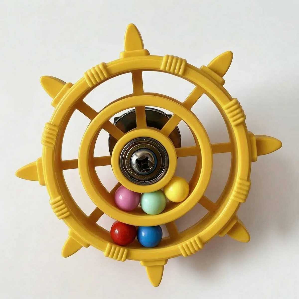 Yellow version of the wheel toy with a metal bearing hub, a dark mount behind and a few coloured balls at the bottom. 6