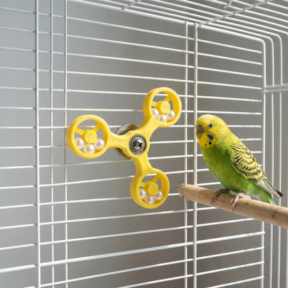 Yellow spinner toy attached to white cage bars while a green budgie sits on a wooden perch next to it. 3