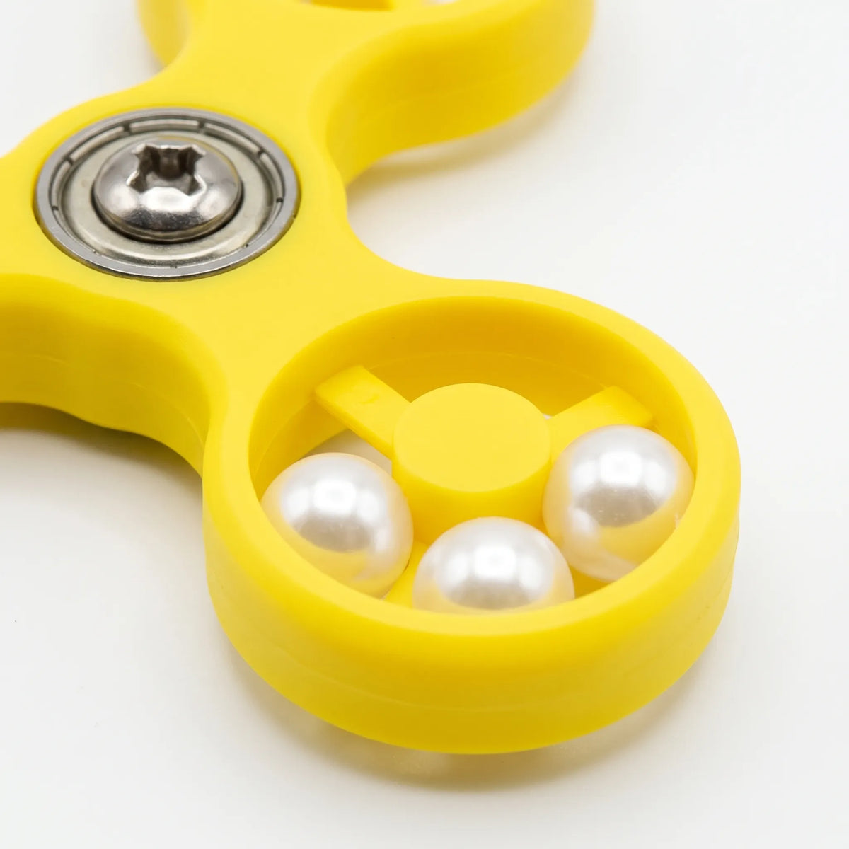 Close-up of one ring of the yellow spinner, showing three glossy white beads, the central hub and the metal bearing screw. 4