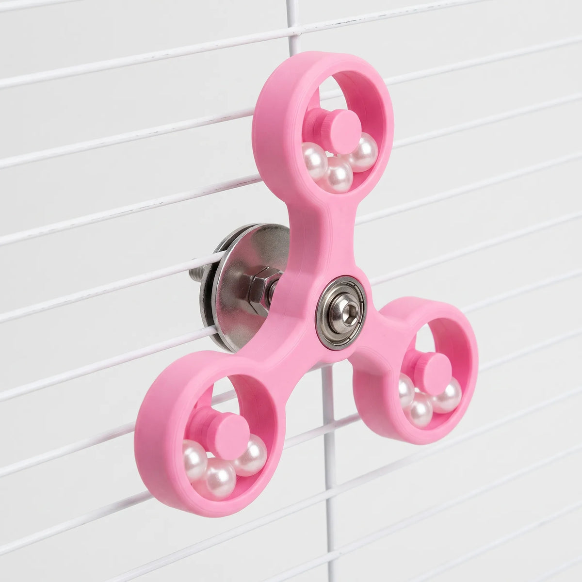 Angled view of the pink version of the spinner clamped to white cage bars, showing the steel washer and nut at the back. 5