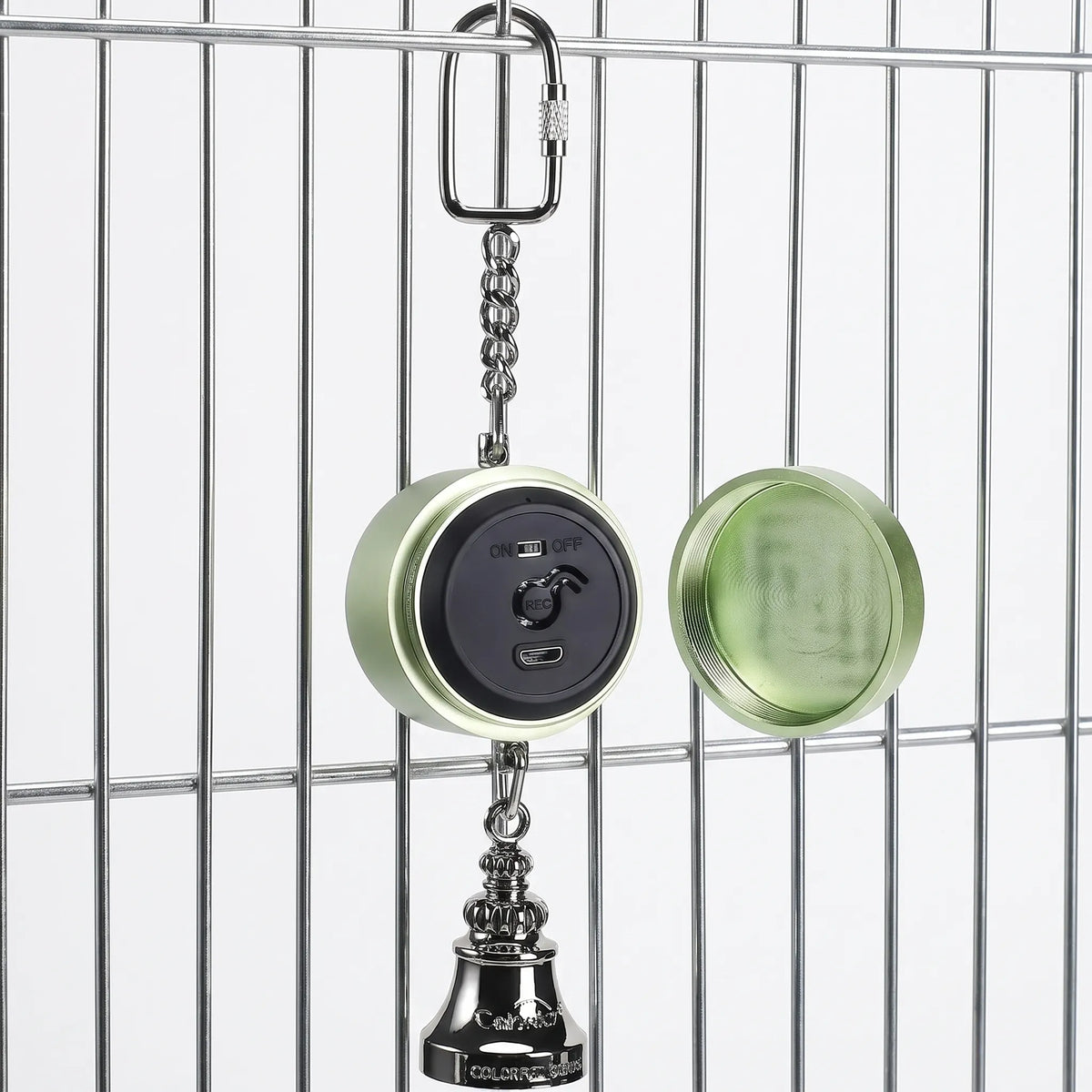 Green version hanging from a cage bar with its screw-off back cover removed beside it, exposing the black control panel and bell below. 4