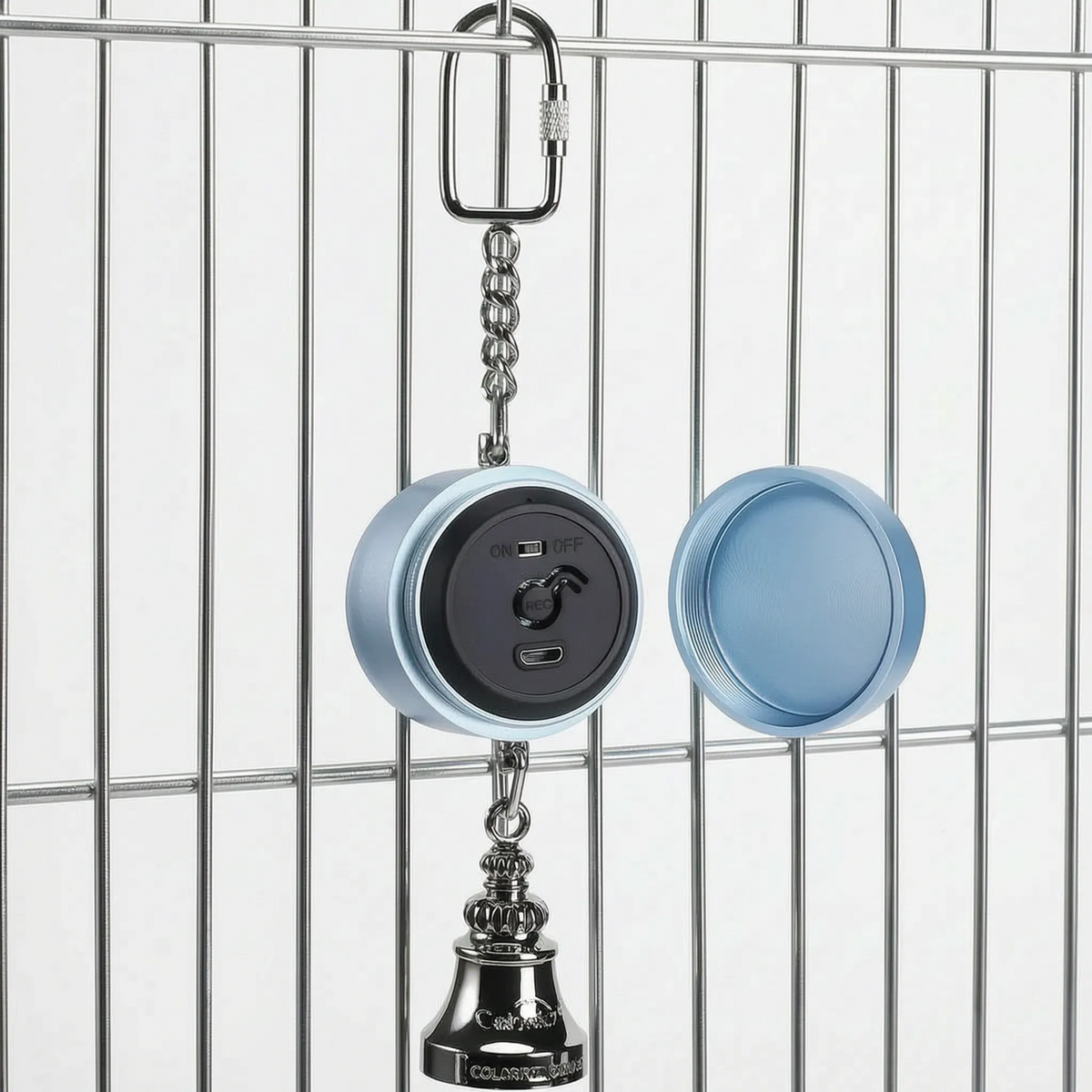 Blue version hanging from a cage bar with its screw-off back cover detached beside it, revealing the black panel with switch, record button and charging port. 5