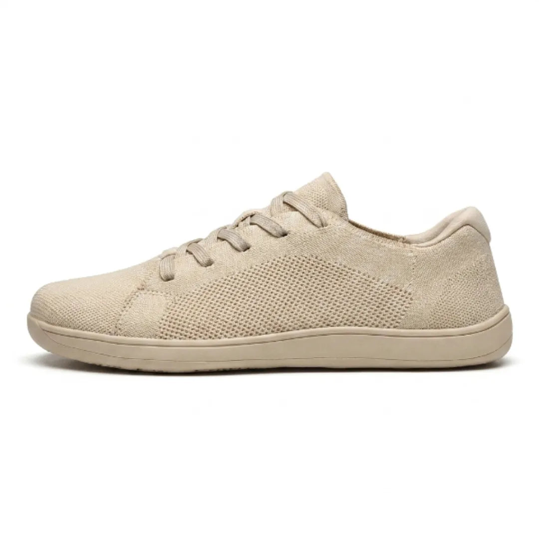 Side view of a beige lace-up knit trainer with a perforated mesh panel and a flat, wide sole. 1