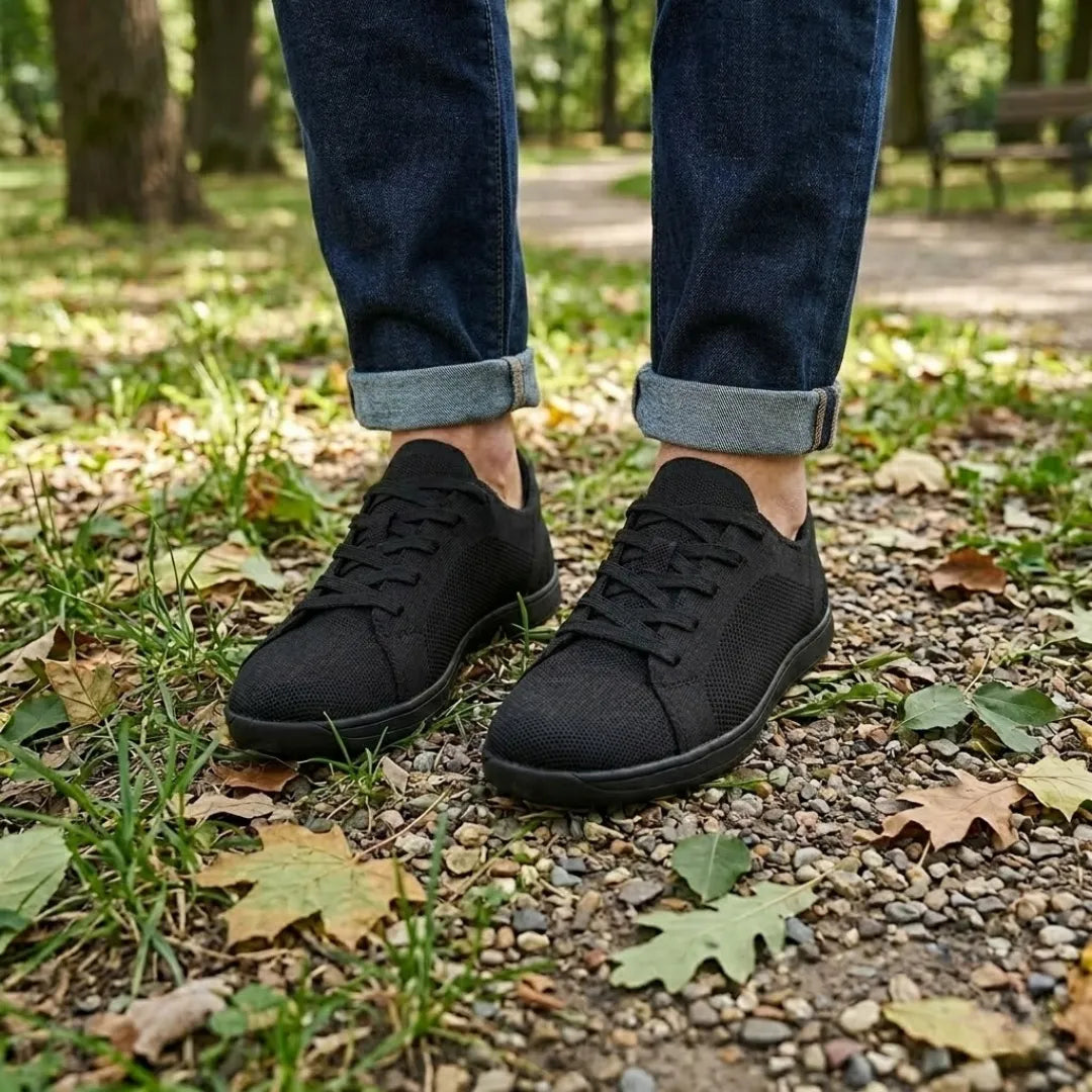 Black trainers worn with rolled dark jeans on a gravel path scattered with autumn leaves. 11