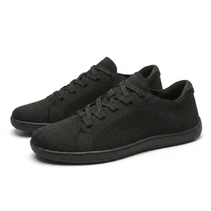 Pair of black knit trainers angled together, showing laces, mesh side panels and flat black soles. 16