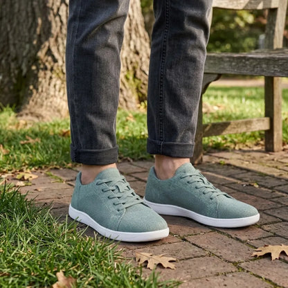 Person wearing sage green mesh trainers with white soles and grey rolled-up jeans, standing on a brick path beside a park bench. 29