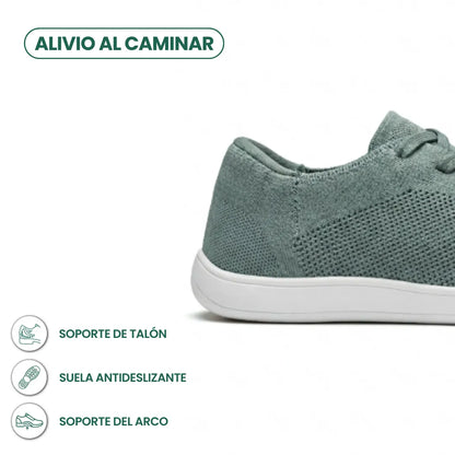 Close-up of the heel and side of a sage green knit trainer on a white sole, with icons for heel, grip and arch support. 31