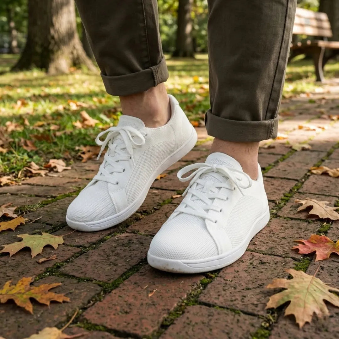 Person wearing white mesh trainers with olive green rolled-up trousers, walking on a brick path strewn with autumn leaves. 38