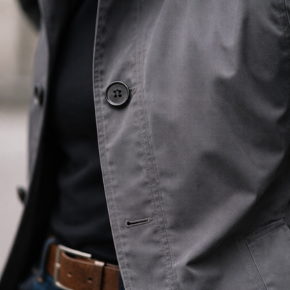 Close-up detail of the grey jacket's dark four-hole button, stitched buttonhole and front placket, with the brown belt below. 8