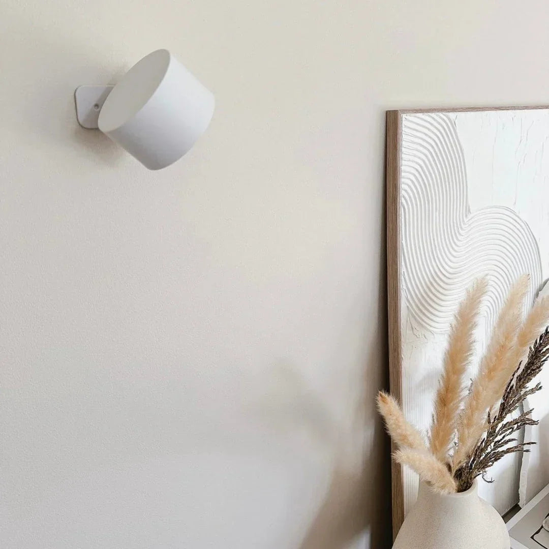 White lamp switched off on a cream wall, beside a textured artwork and dried pampas grass 16