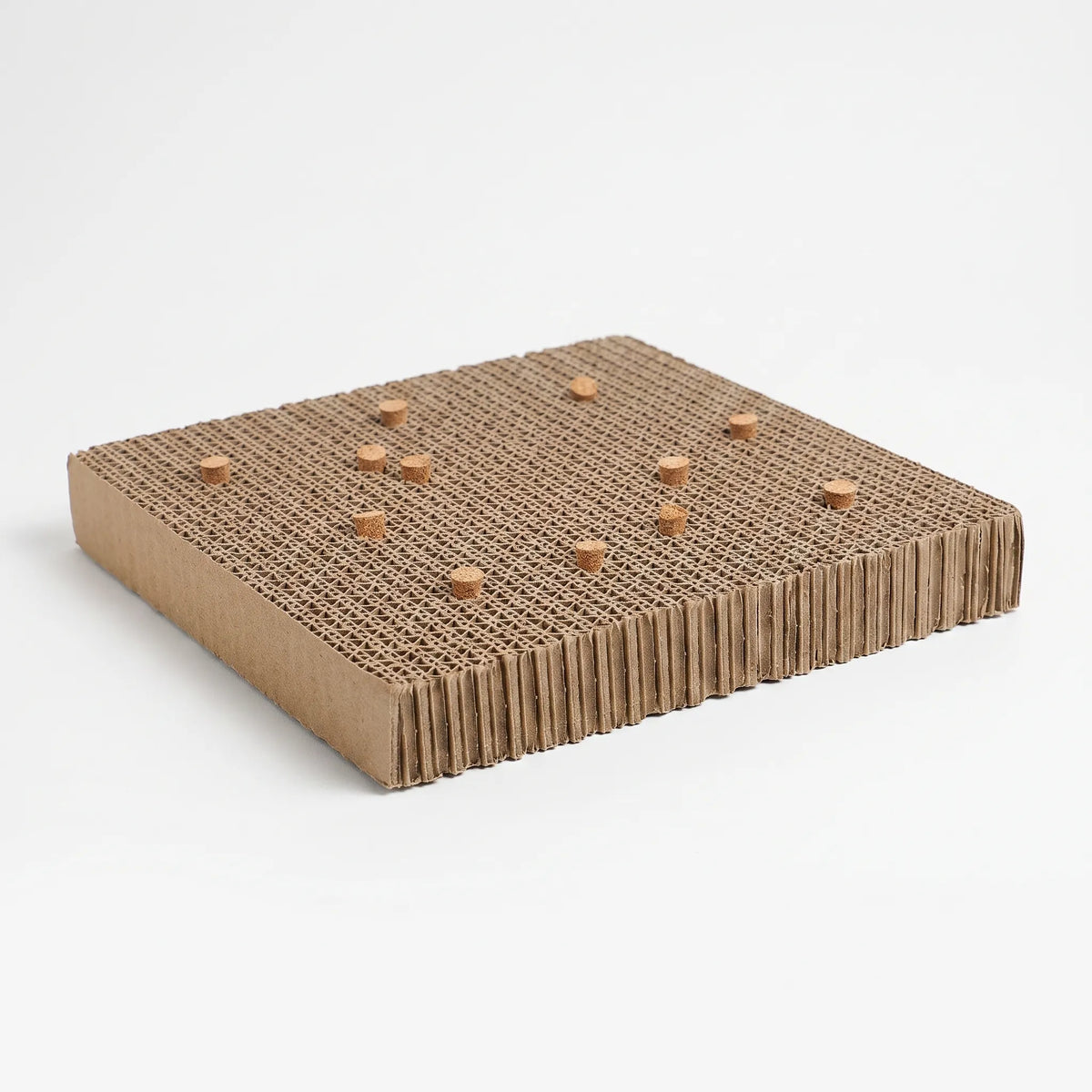 Corrugated cardboard platform seen at an angle, with small cork stoppers pushed into the layered top surface, on a plain white background. 1