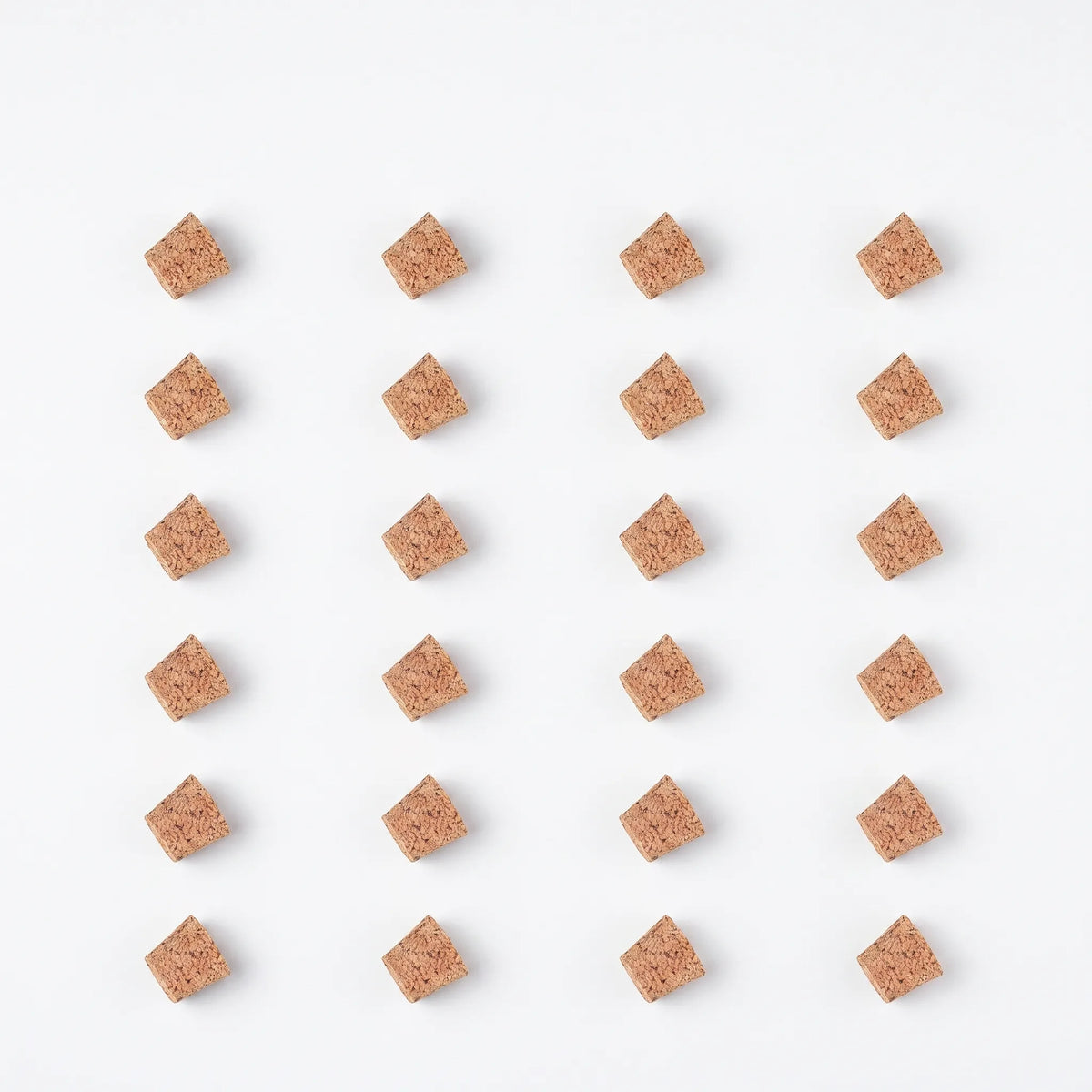 Flat lay of twenty-four tapered cork stoppers in a neat grid of six rows and four columns on a white background. 9