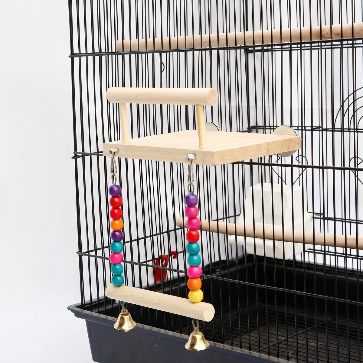 Wooden platform with a perch bar and a bead-and-bell swing, fitted to the side of a black cage. 1