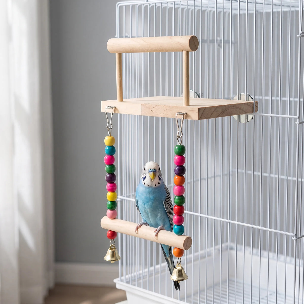 A blue budgerigar perched on the hanging swing of the wooden platform, which is attached to a white cage. 2